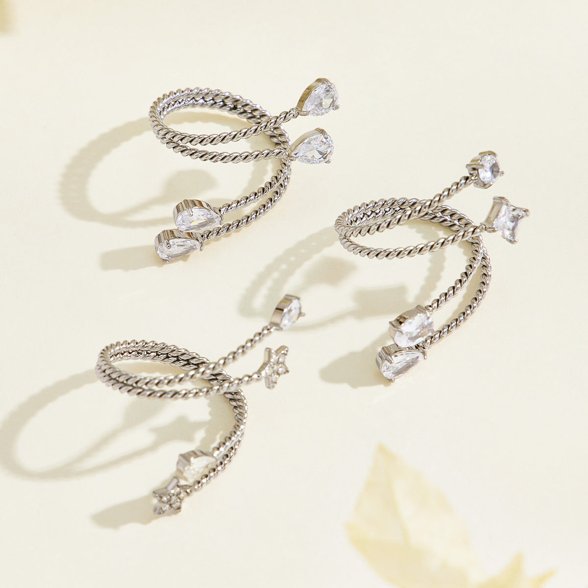 Steel-tone stainless steel twisted open rings arranged on a cream surface, showing clear stones and decorative end details