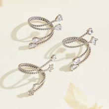 Steel-tone stainless steel twisted open rings arranged on a cream surface, showing clear stones and decorative end details
