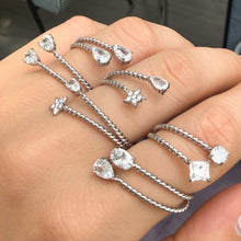 Steel-tone stainless steel twisted open rings worn on fingers with clear stones and star, square and teardrop accents