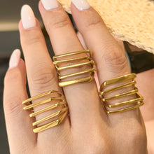 Three gold-tone stainless steel openwork rings worn on adjacent fingers beside a woven accessory