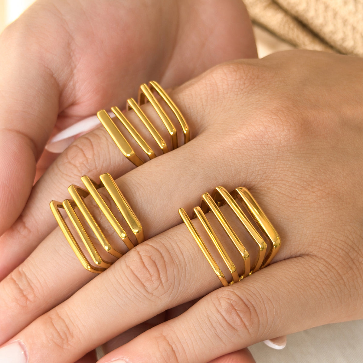 Three gold-tone stainless steel statement rings worn on angled fingers, showing the parallel-bar faces