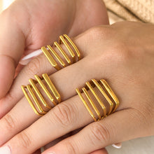 Three gold-tone stainless steel statement rings worn on angled fingers, showing the parallel-bar faces