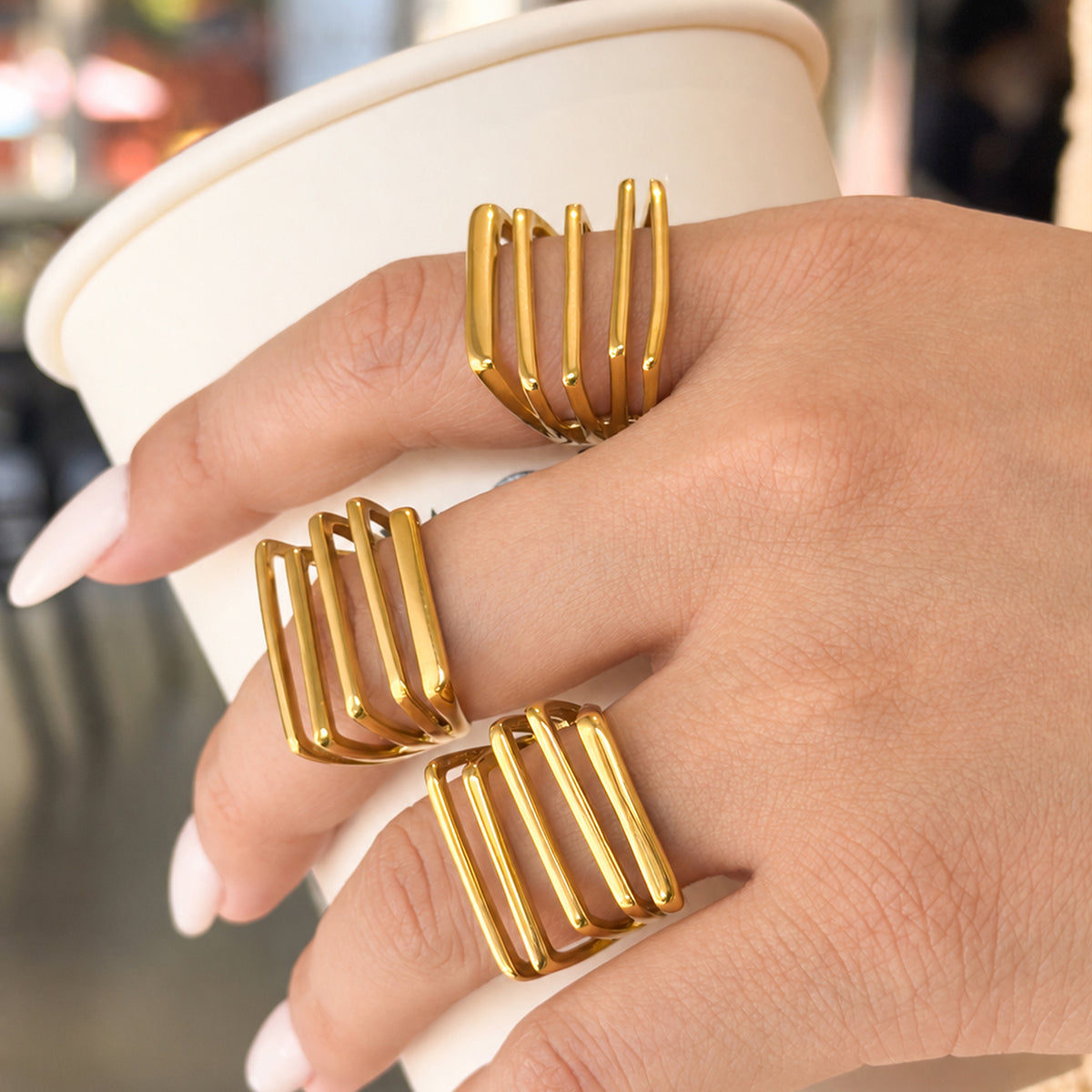 Side view of three gold-tone stainless steel statement rings worn on fingers, showing the raised parallel bars