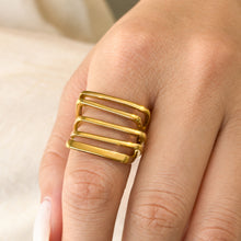 Close-up of a gold-tone stainless steel wide band ring worn on a finger, showing its parallel bars