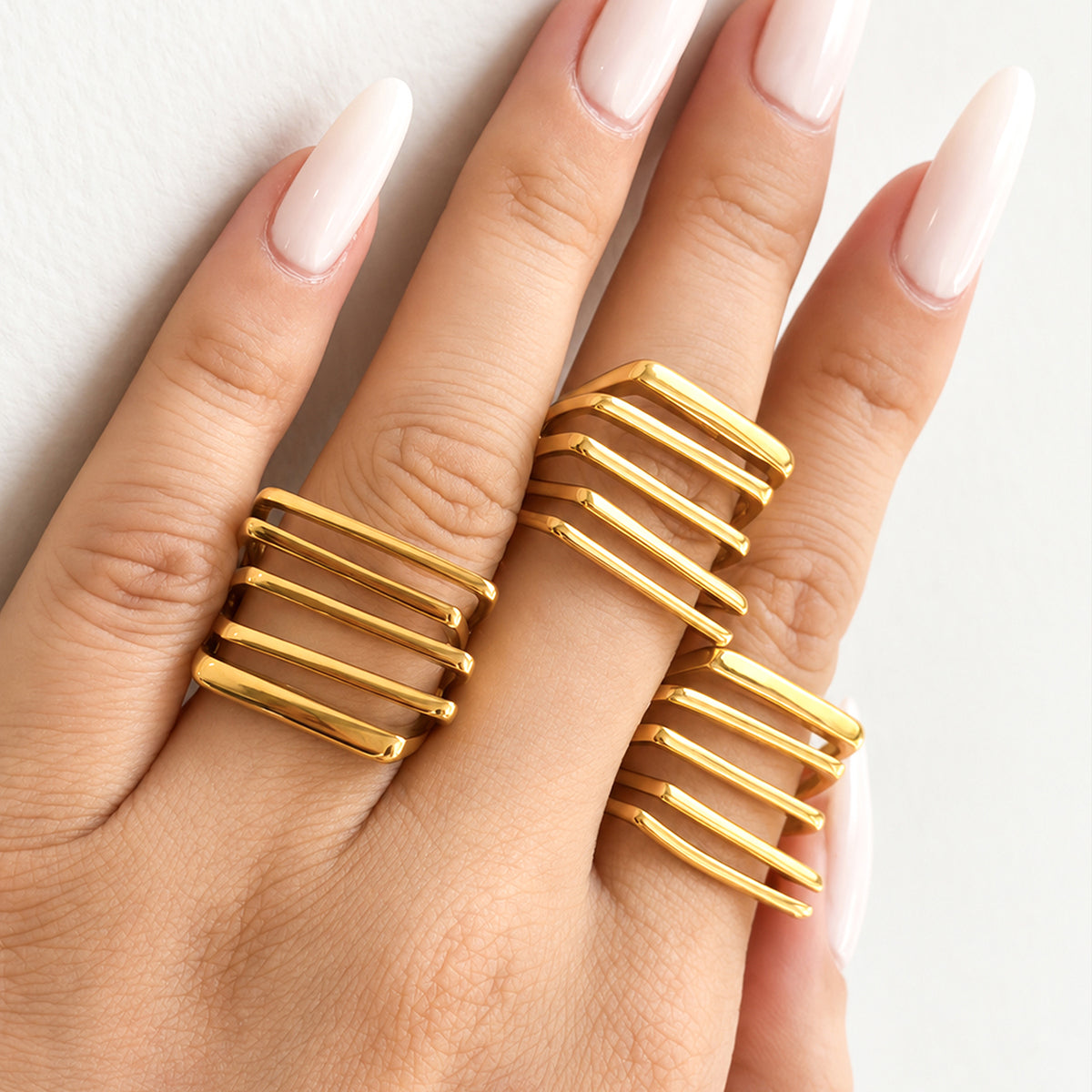 Three gold-tone stainless steel multi-row rings worn on a hand with long white nails