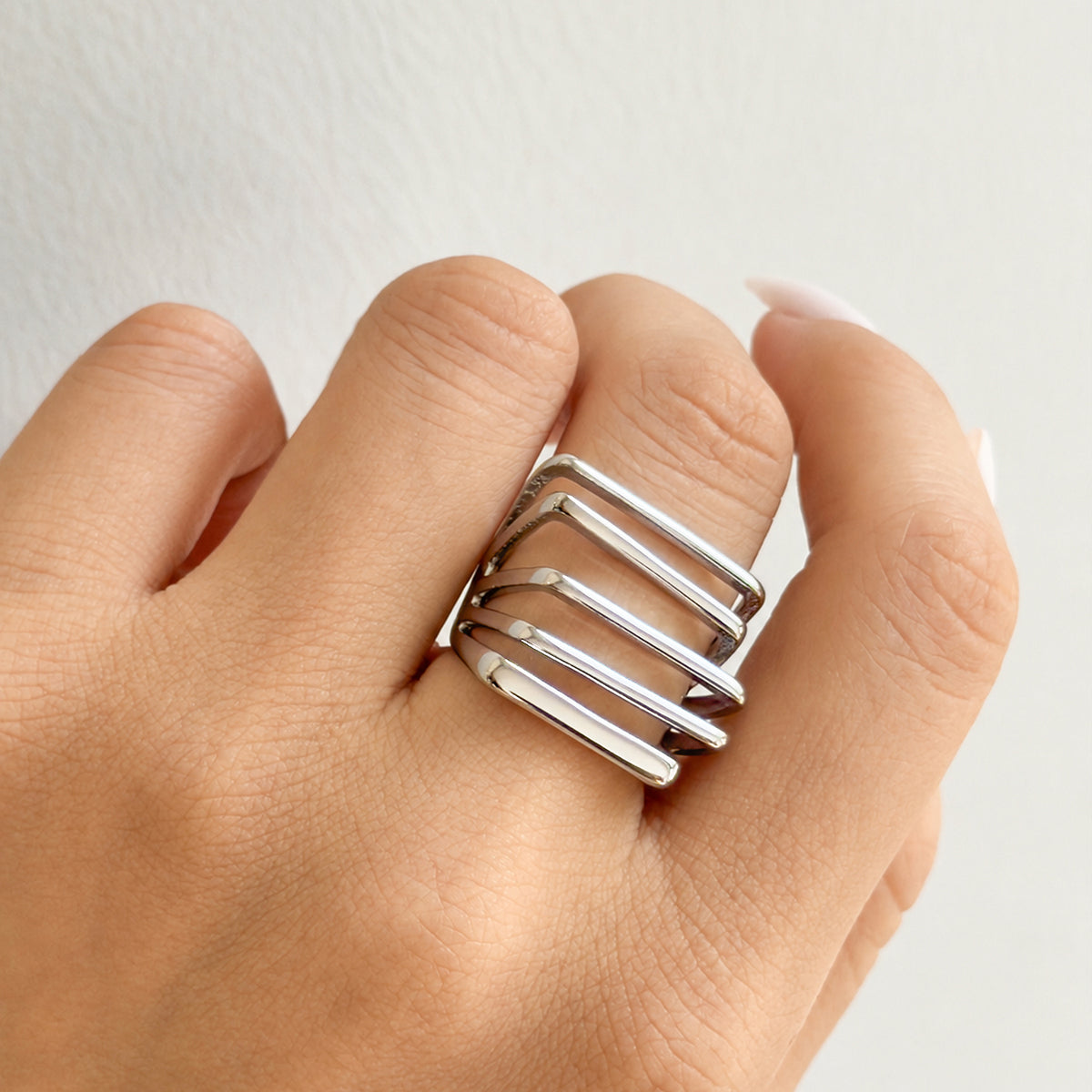 Steel-tone stainless steel openwork statement ring worn on a curled hand, showing its polished geometric face