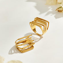 Two gold-tone stainless steel openwork rings displayed upright and flat with white flowers in the background