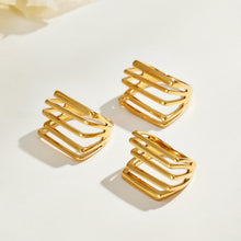 Three gold-tone stainless steel multi-row statement rings arranged in a triangular layout on a light surface