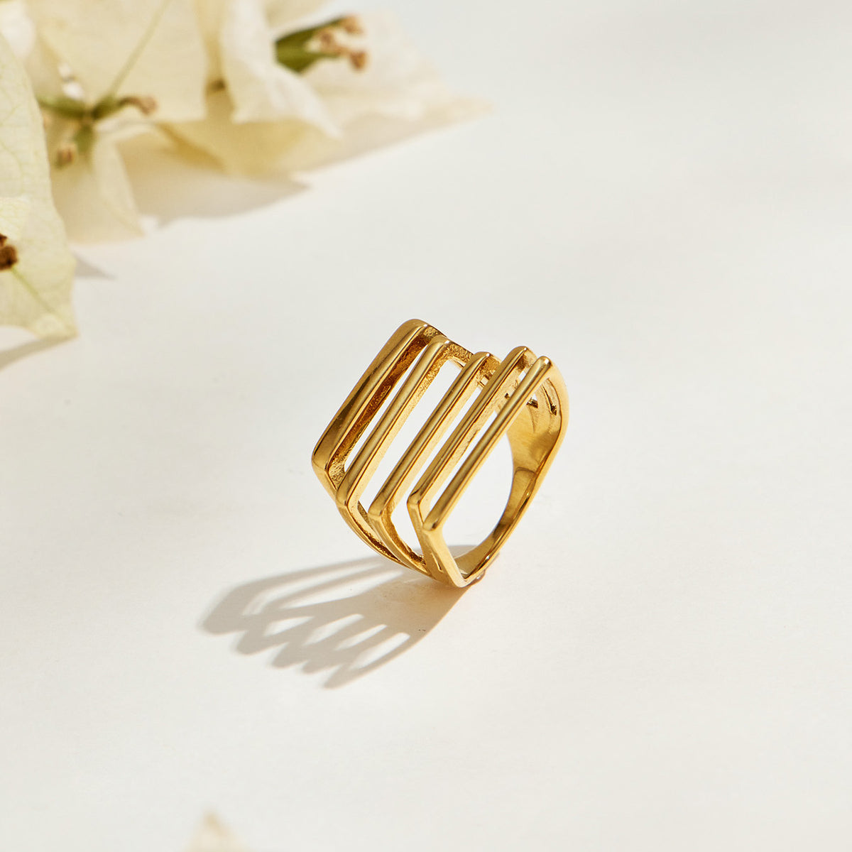 Gold-tone stainless steel multi-row ring standing at an angle, showing its openwork face and cast shadow