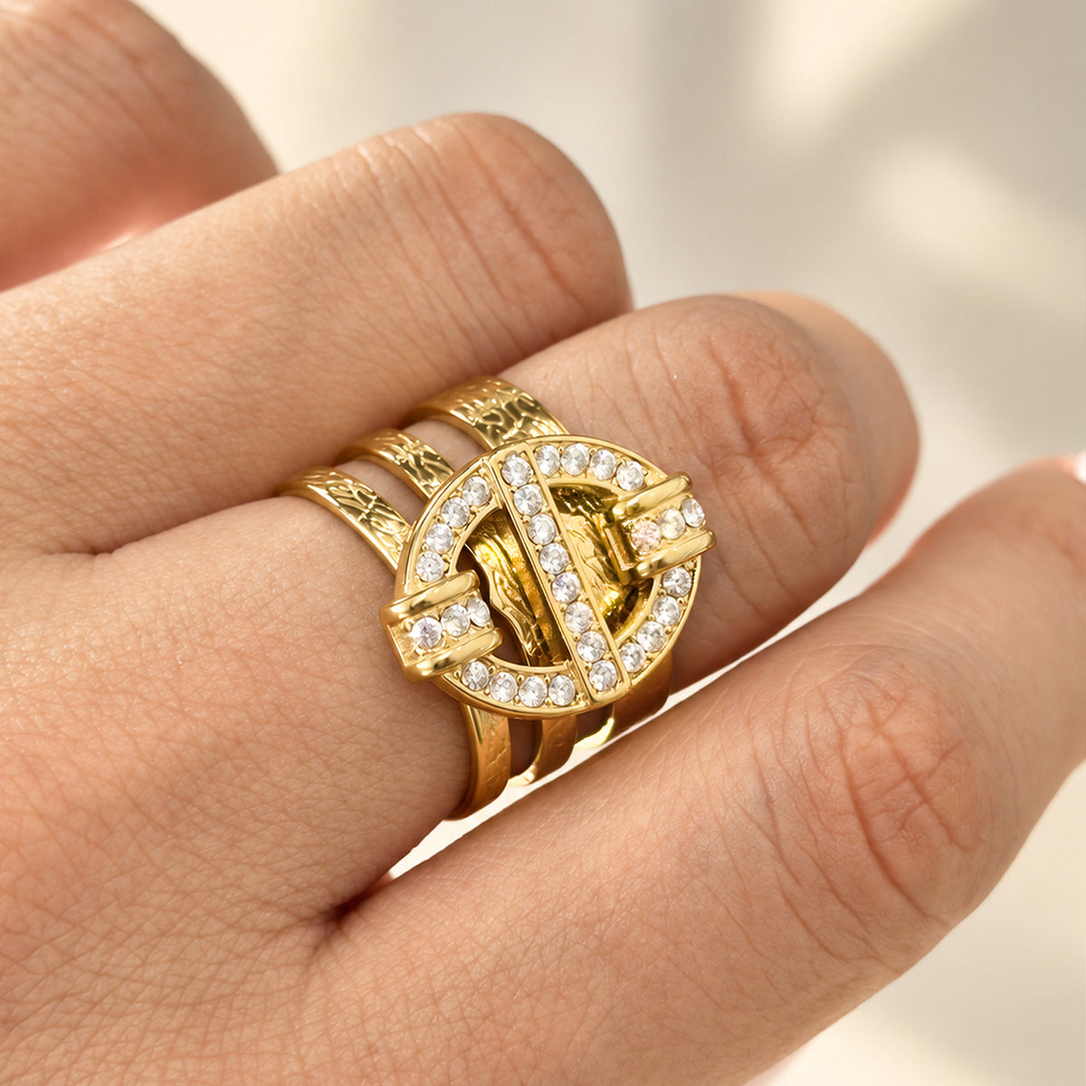 Close-up of the A413 gold-tone stainless steel geometric ring worn on a finger, showing its openwork motif and clear stones