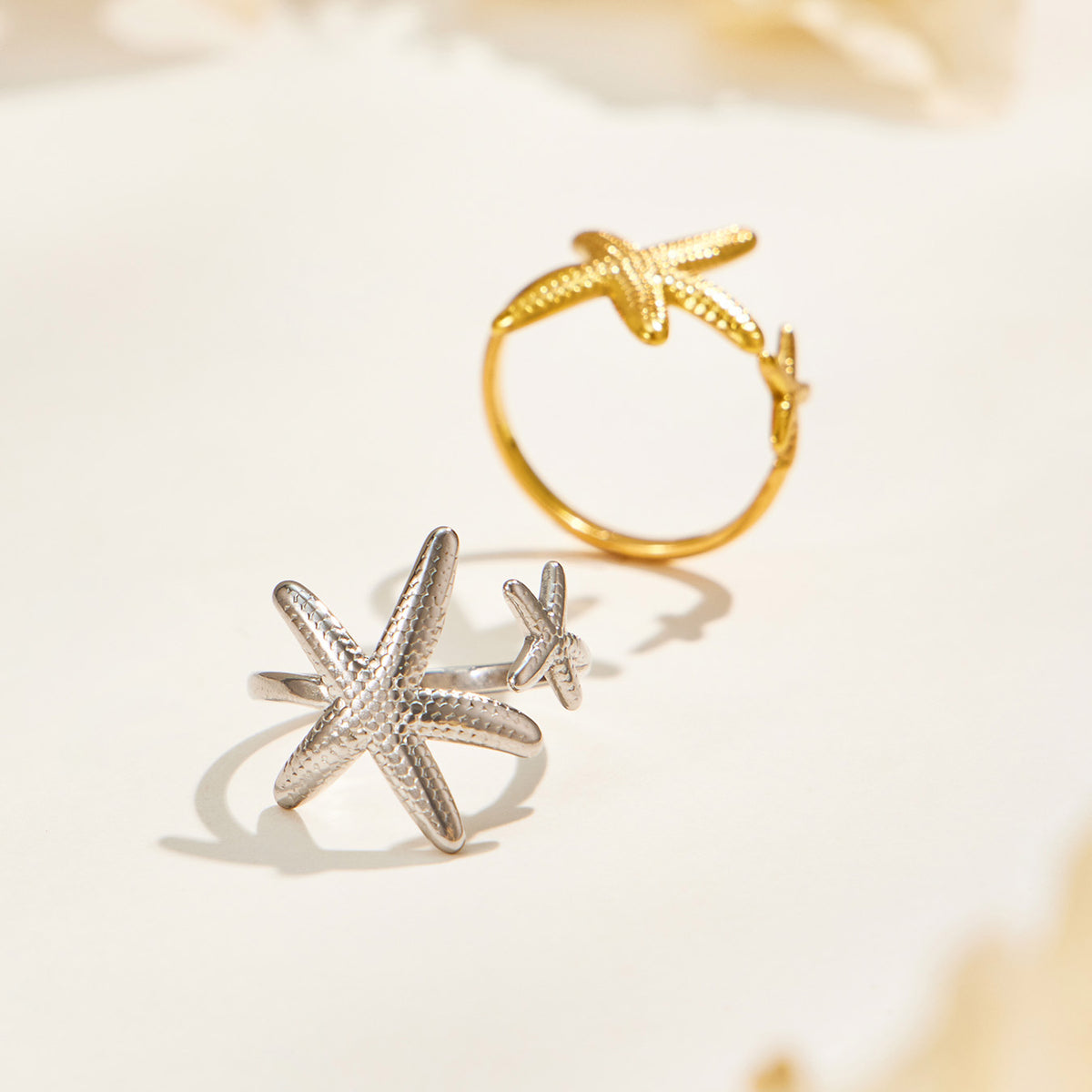 Gold and silver starfish open rings displayed on a light background, showing the contrasting finishes and textured designs