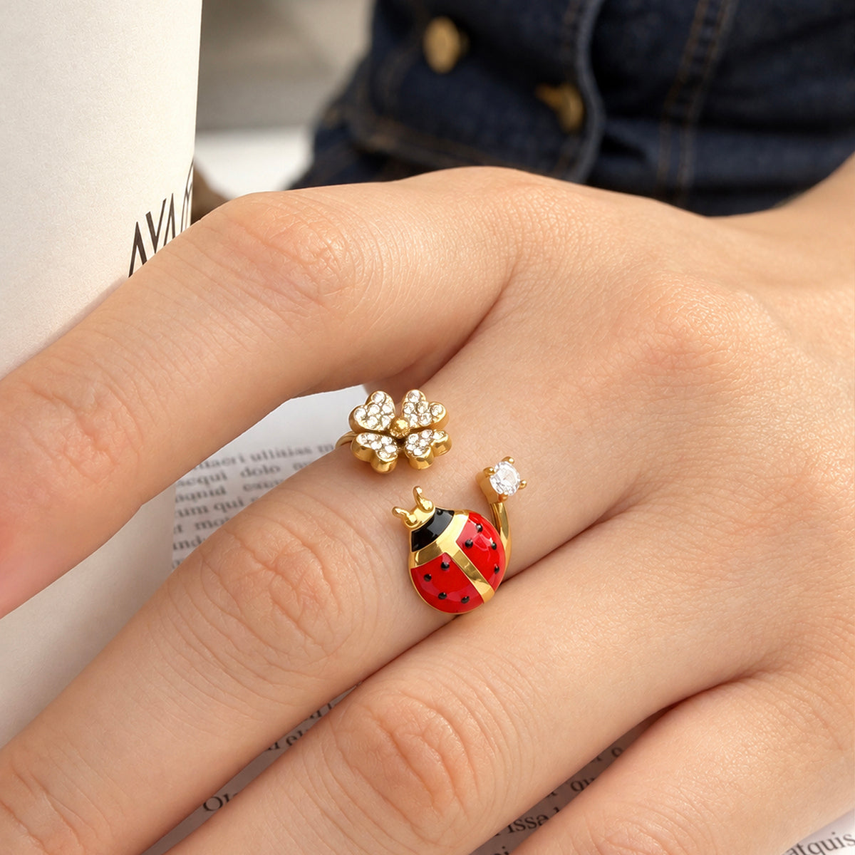 A445 gold-tone stainless steel open ring worn on a finger, featuring a red-and-black ladybug, a flower and clear stone accents