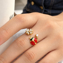 A445 gold-tone stainless steel open ring worn on a finger, featuring a red-and-black ladybug, a flower and clear stone accents
