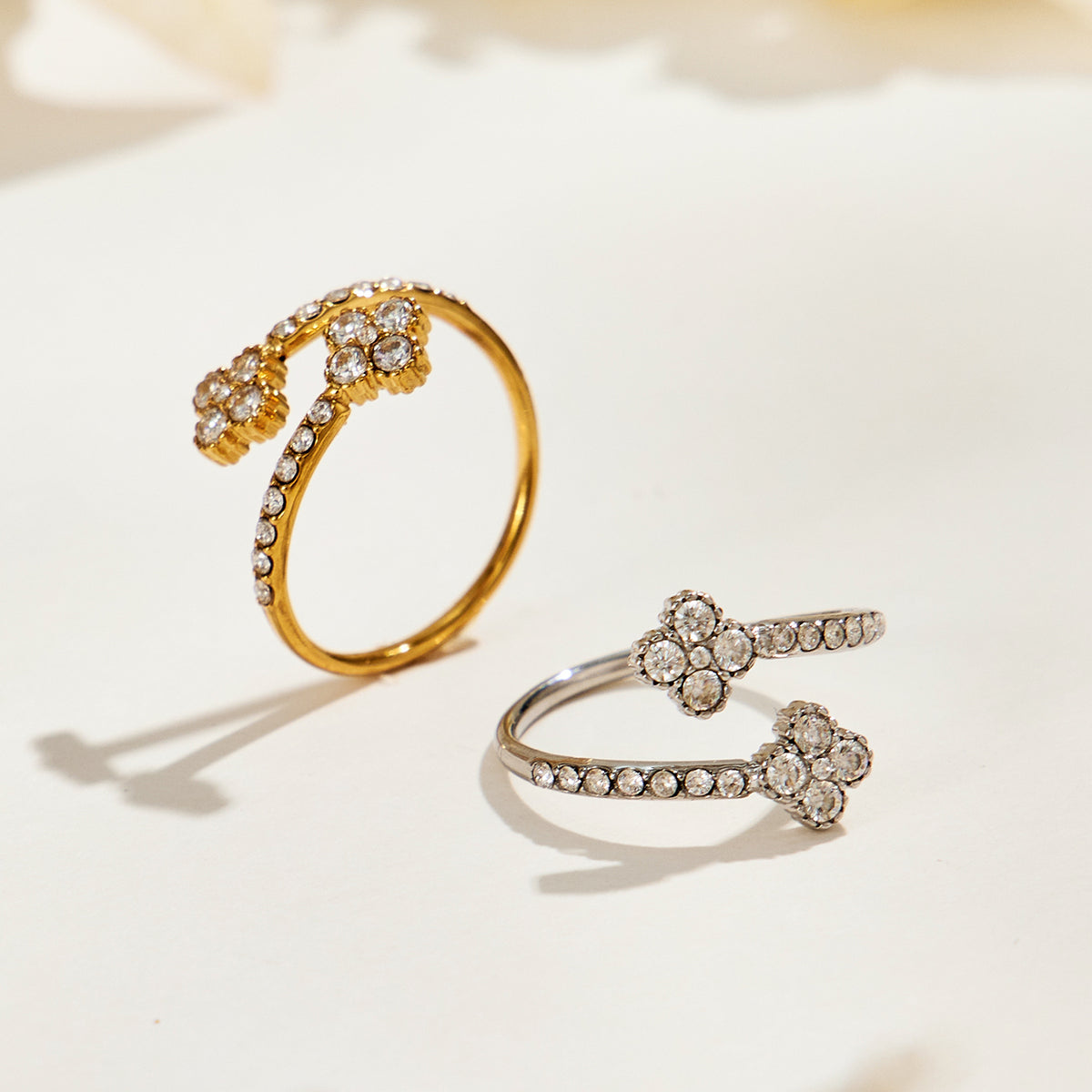 Gold-tone and steel-tone A446 stainless steel double-flower open rings displayed together on a cream surface