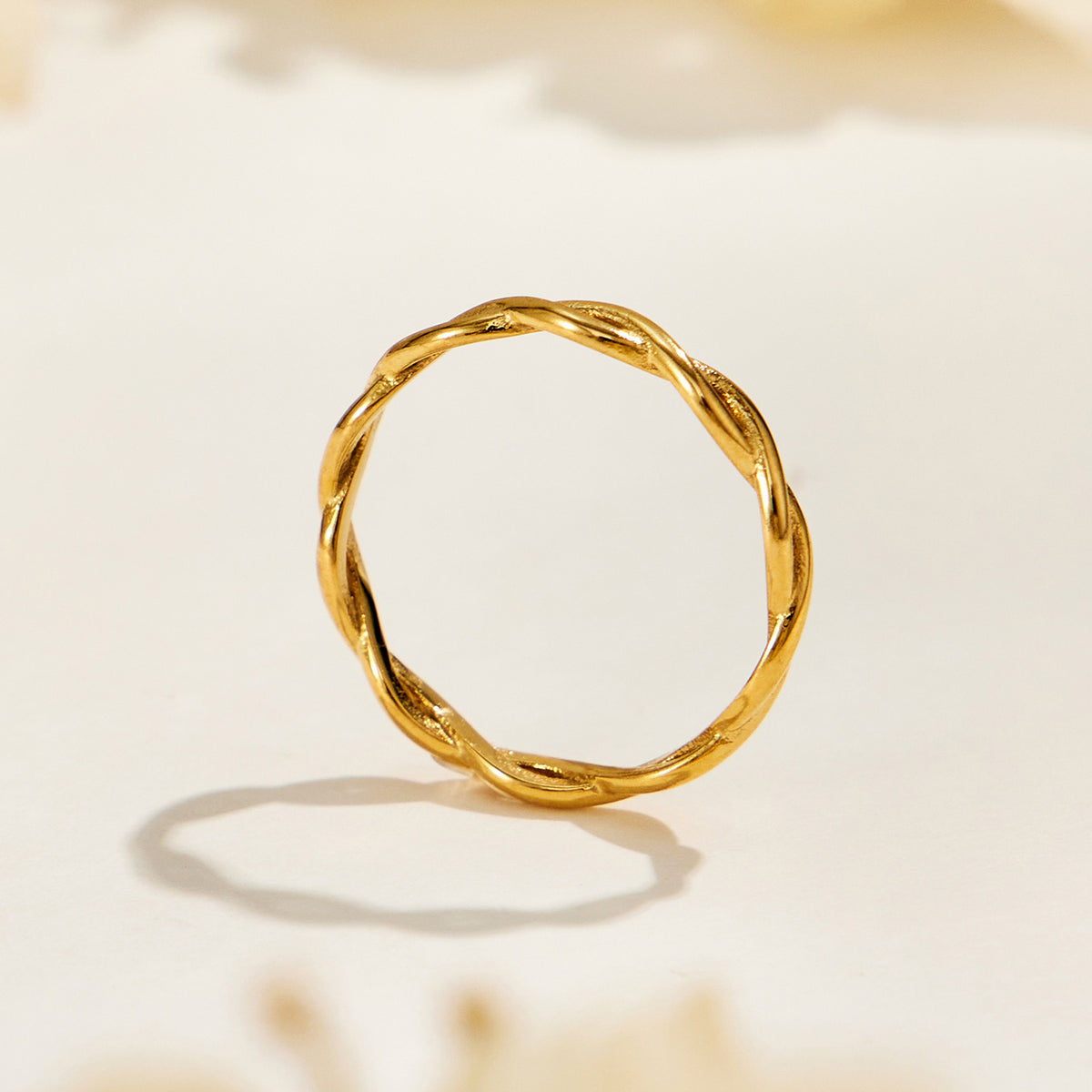 A451 gold-tone stainless steel twisted band ring standing upright on a cream surface, showing its closed circular band