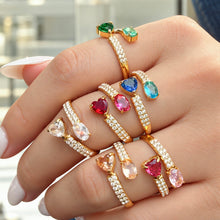 Colorful gold-tone stainless steel open rings worn across the fingers, showing heart and oval stones with clear-stone bands