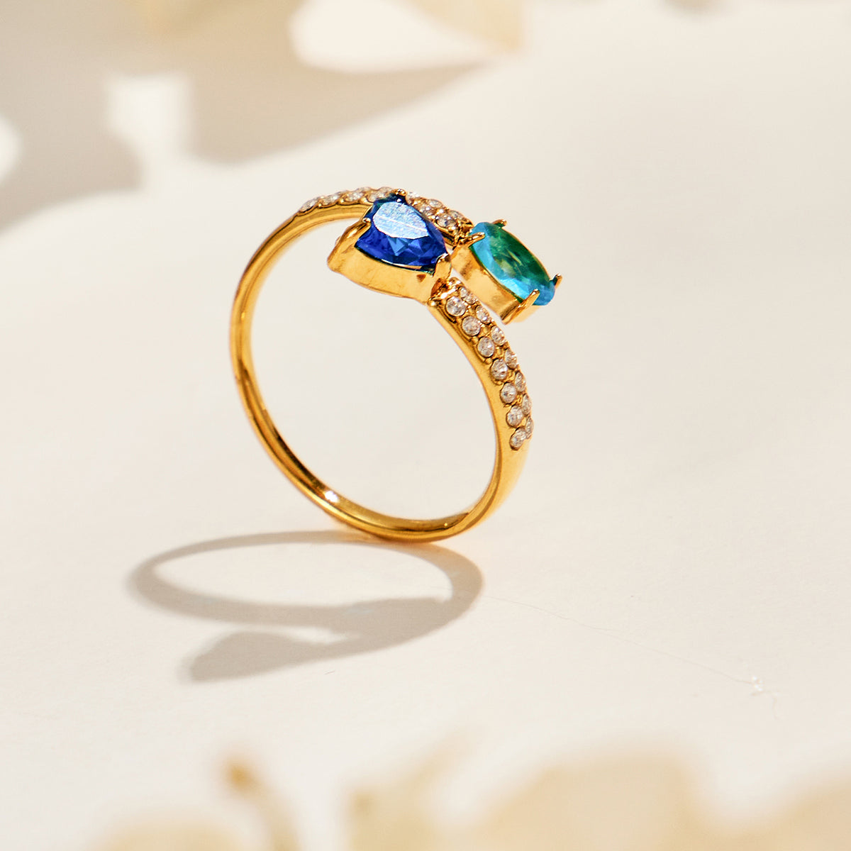 Gold-tone stainless steel ring standing upright with a blue heart stone, teal oval stone and sparkling open band