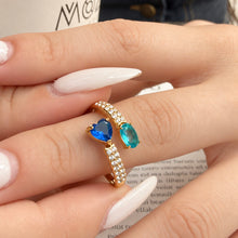 Gold-tone stainless steel open ring worn on a finger with a blue heart stone, teal oval stone and clear-stone band
