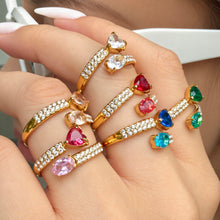 Gold-tone stainless steel heart and oval cubic zirconia rings styled together across a hand