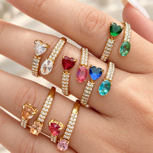Close-up of gold-tone stainless steel rings worn on fingers, highlighting the heart and oval stones and rows of small clear stones