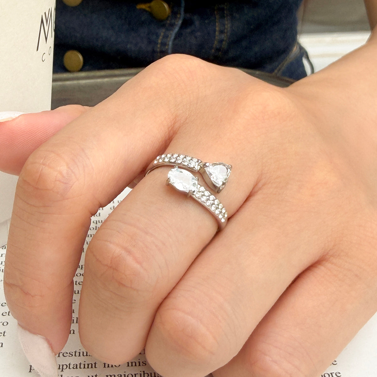 Steel-tone stainless steel heart and oval cubic zirconia open ring worn on a finger with clear stones