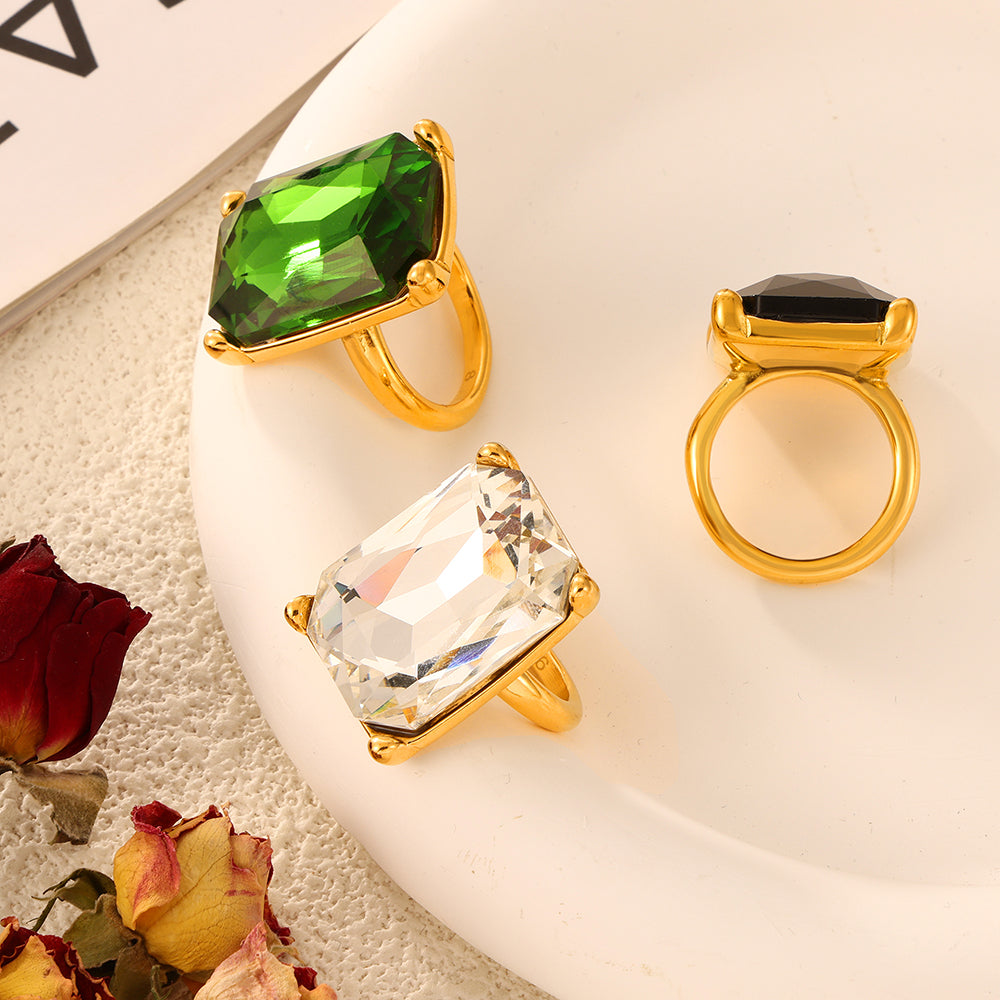 A590 gold-tone rectangular stone cocktail rings in green, clear and black arranged on a white tray