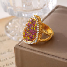 Gold-tone multicolor teardrop ring displayed upright on a taupe box, showing its raised setting and textured band.
