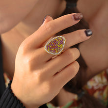 Three-quarter view of a gold-tone multicolor teardrop ring worn on a model's finger near her shoulder.
