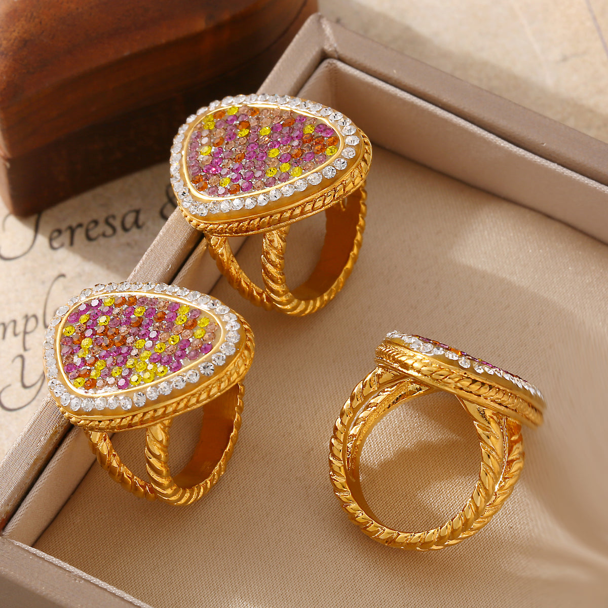 Three gold-tone teardrop rings displayed in a beige jewelry box, including a side view of the textured band.