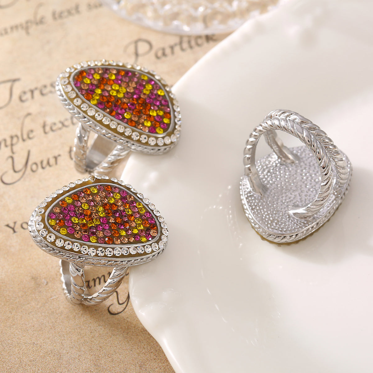 Two steel-tone multicolor teardrop rings shown from the front beside a third ring displaying its underside and band.