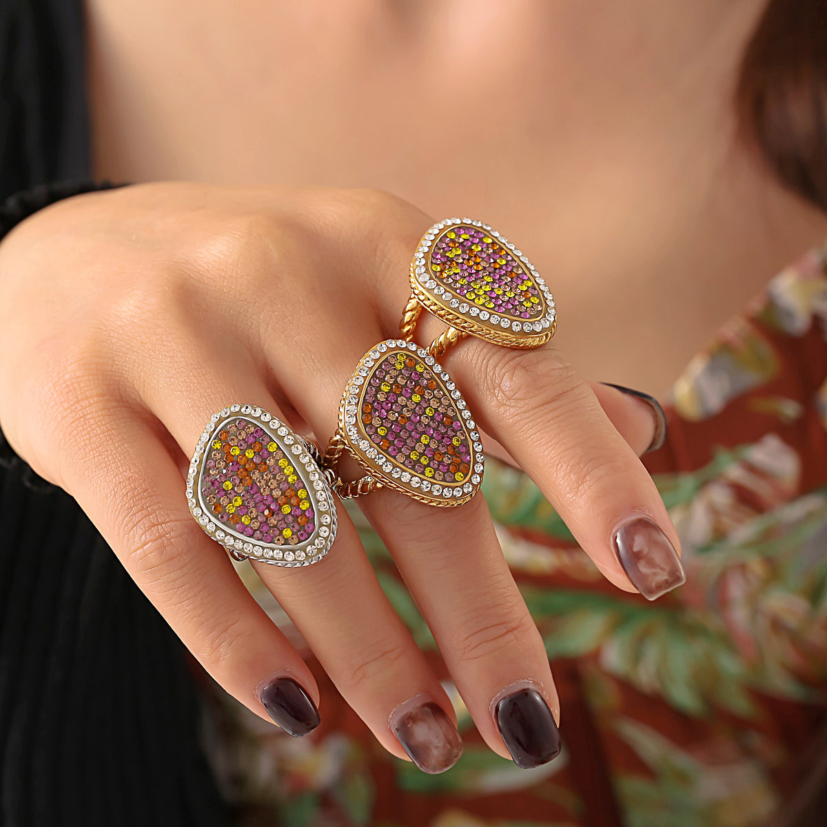 Three multicolor teardrop statement rings worn across a model's fingers against patterned clothing.