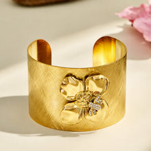 Front view of a wide gold cuff bracelet with a raised bee and flower motif