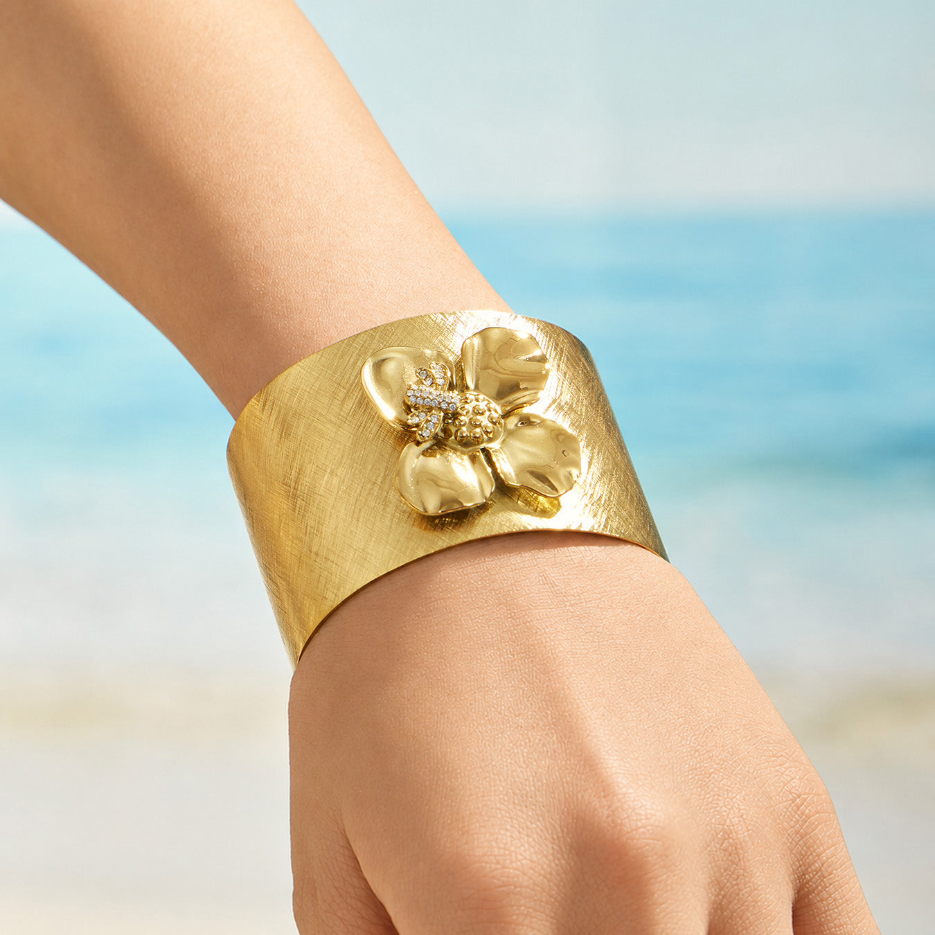 Gold bee flower statement cuff bracelet worn on a model wrist at the beach