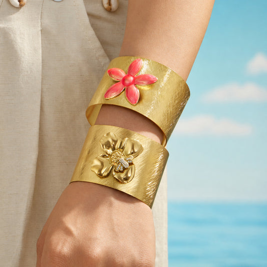 Bee and pink flower gold cuff bracelets stacked on a model wrist by the sea