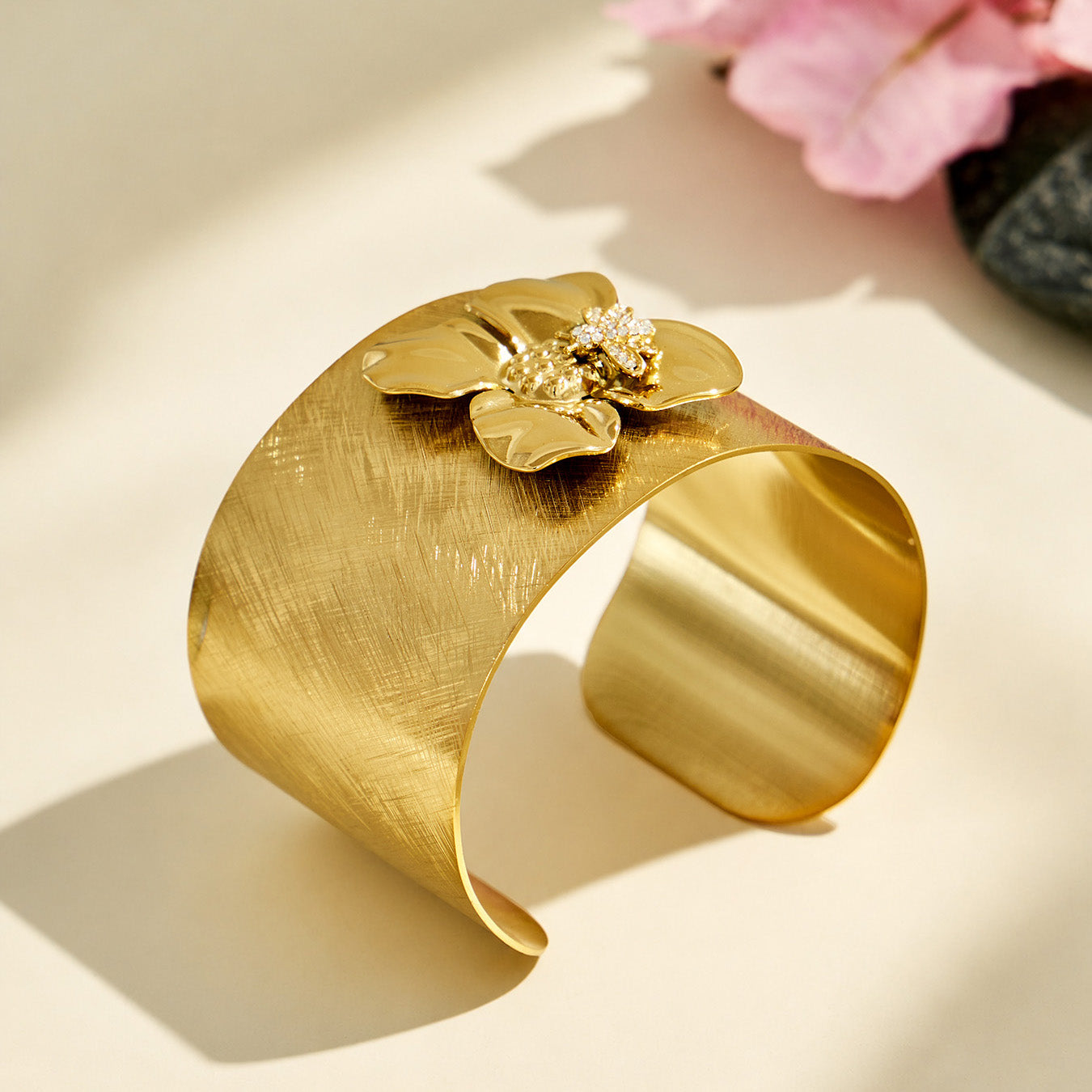 Angled view of a brushed gold cuff bracelet with a sculptural bee flower design