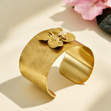 Angled view of a brushed gold cuff bracelet with a sculptural bee flower design