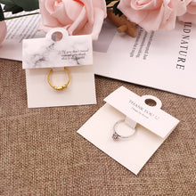 Black and white ring display cards arranged with jewelry on a neutral fabric background