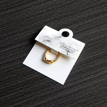 White marble-style ring card displaying a gold-tone ring on a dark surface