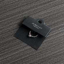 Black ring display card holding a ring on a dark tabletop