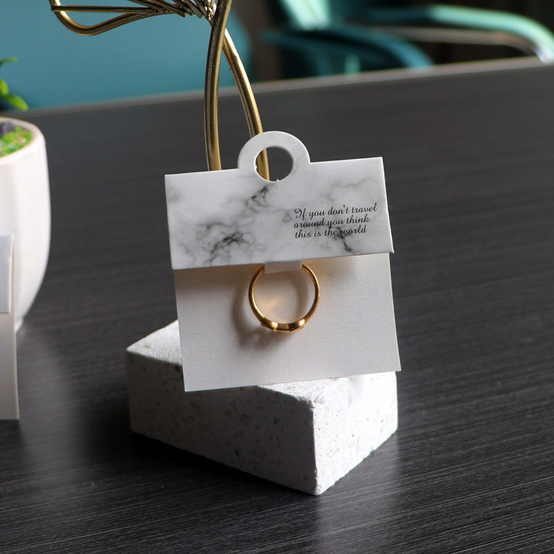 White marble-style ring display card holding a gold-tone ring