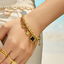 Black four-leaf clover charm bracelet with gold dangling accents worn on the wrist