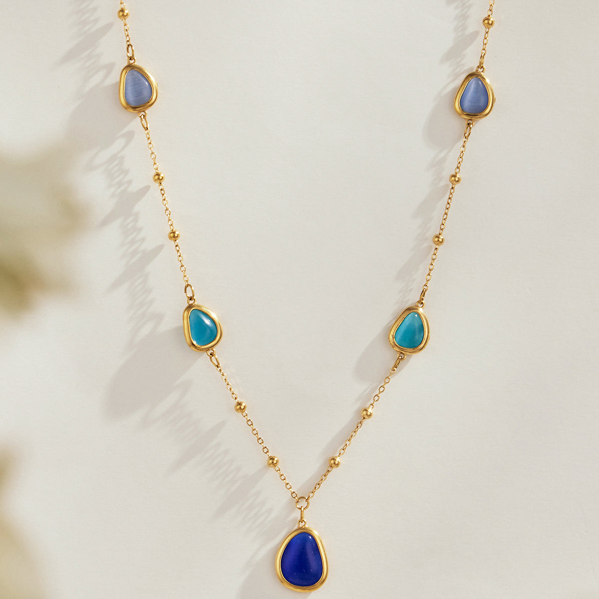 Gold-tone necklace with blue cat eye stones and teardrop pendant detail