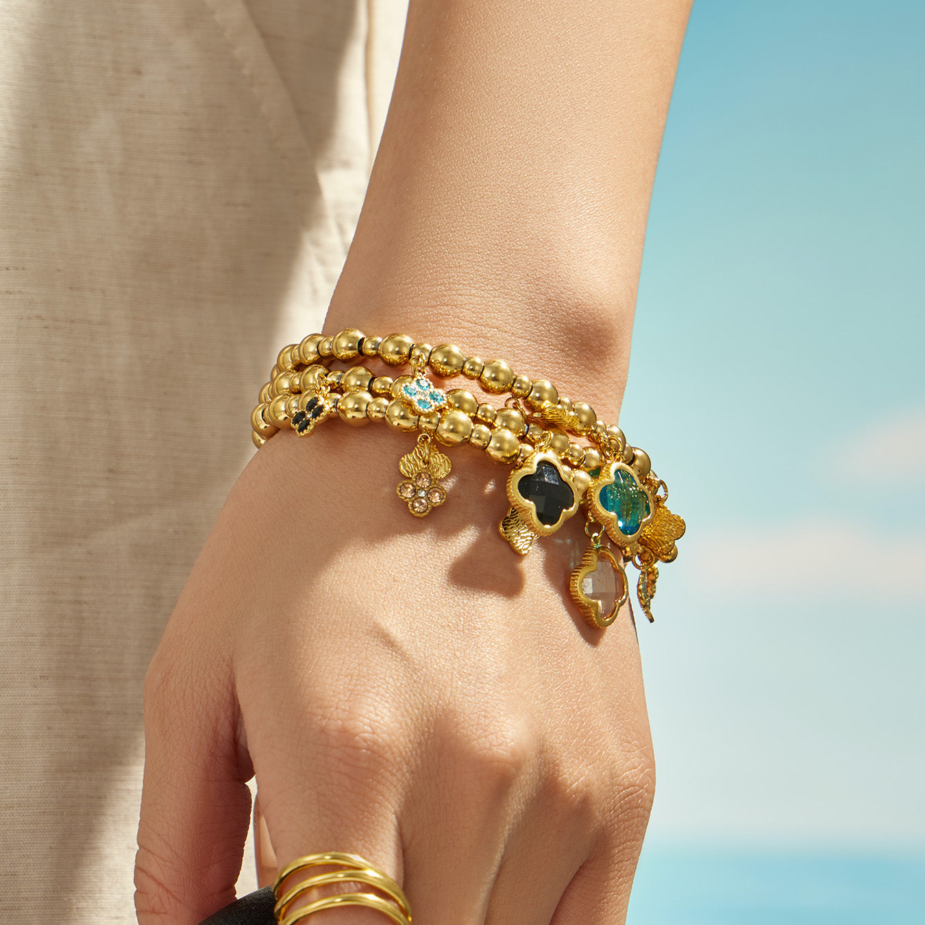 Blue clover charm bracelet styled on a model wrist with a gold beaded chain