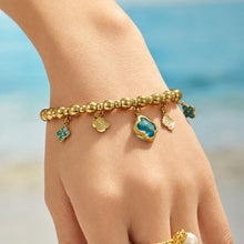 Blue four-leaf clover charm bracelet worn on a model wrist near the beach