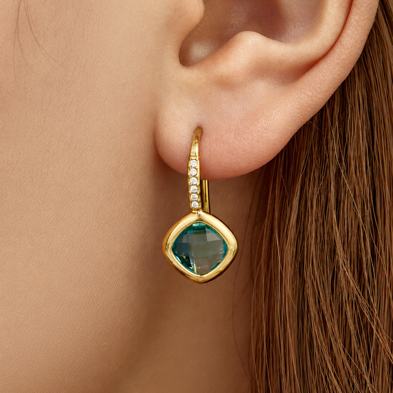 Model wearing blue glass stone drop earrings with faceted geometric detail