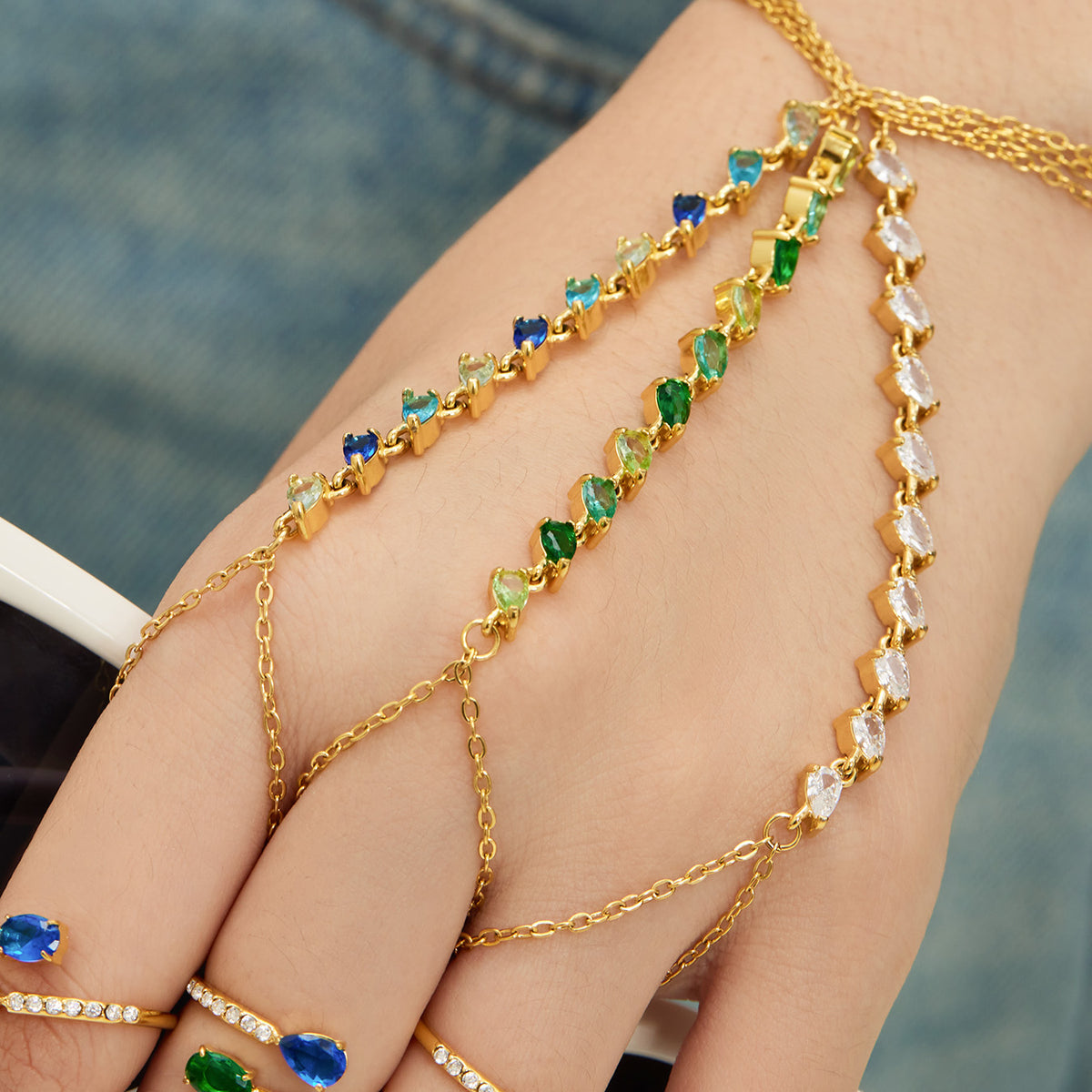 Blue, green and clear CZ hand chain bracelets in gold tone worn together across the hand
