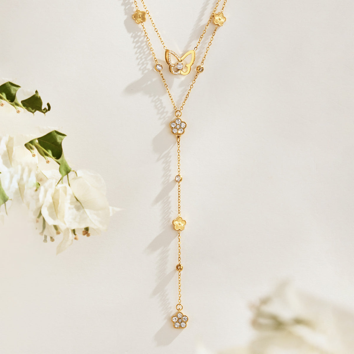 Gold-tone butterfly and floral Y necklaces displayed with white flowers