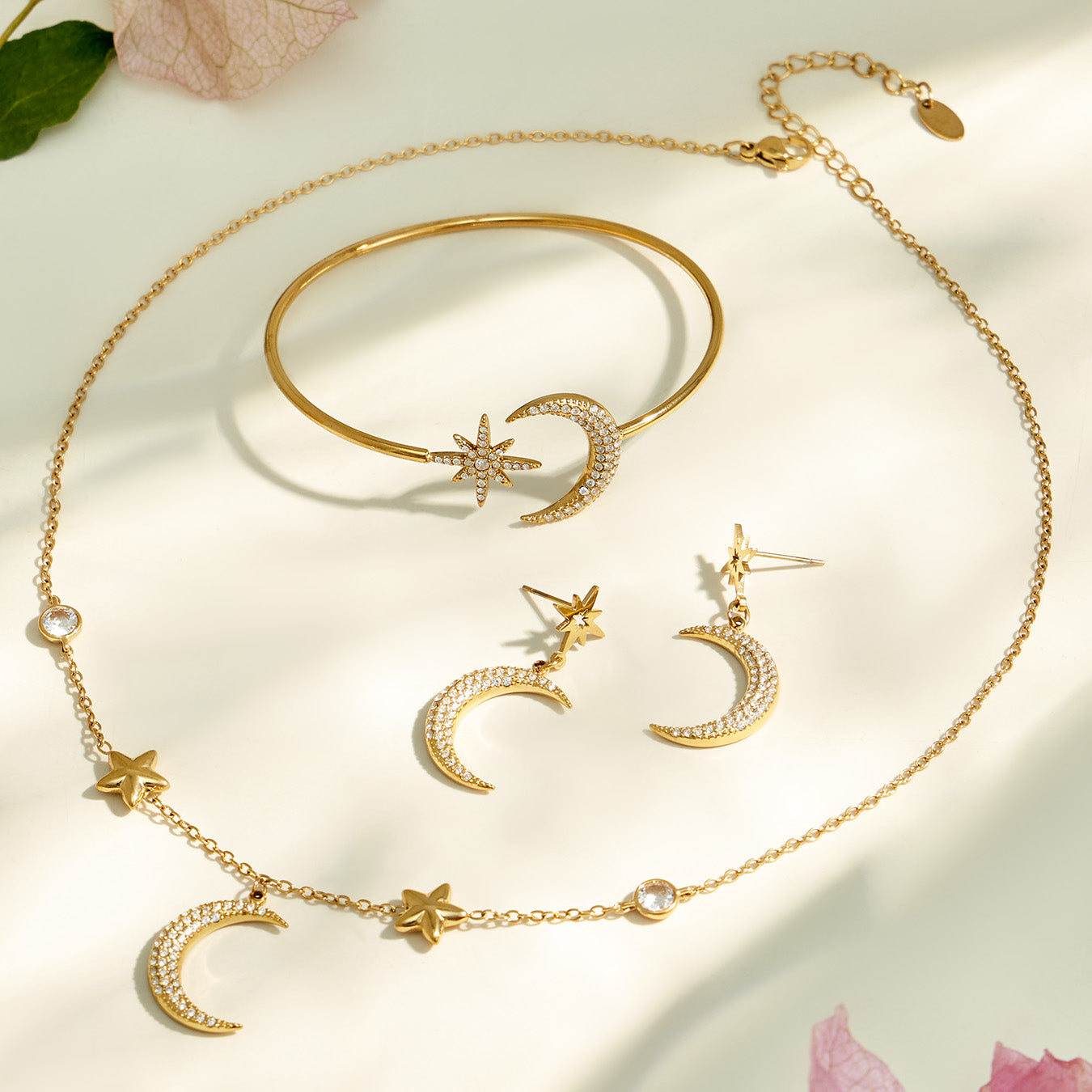 Gold celestial necklace, earrings and cuff bracelet displayed together with star and moon motifs