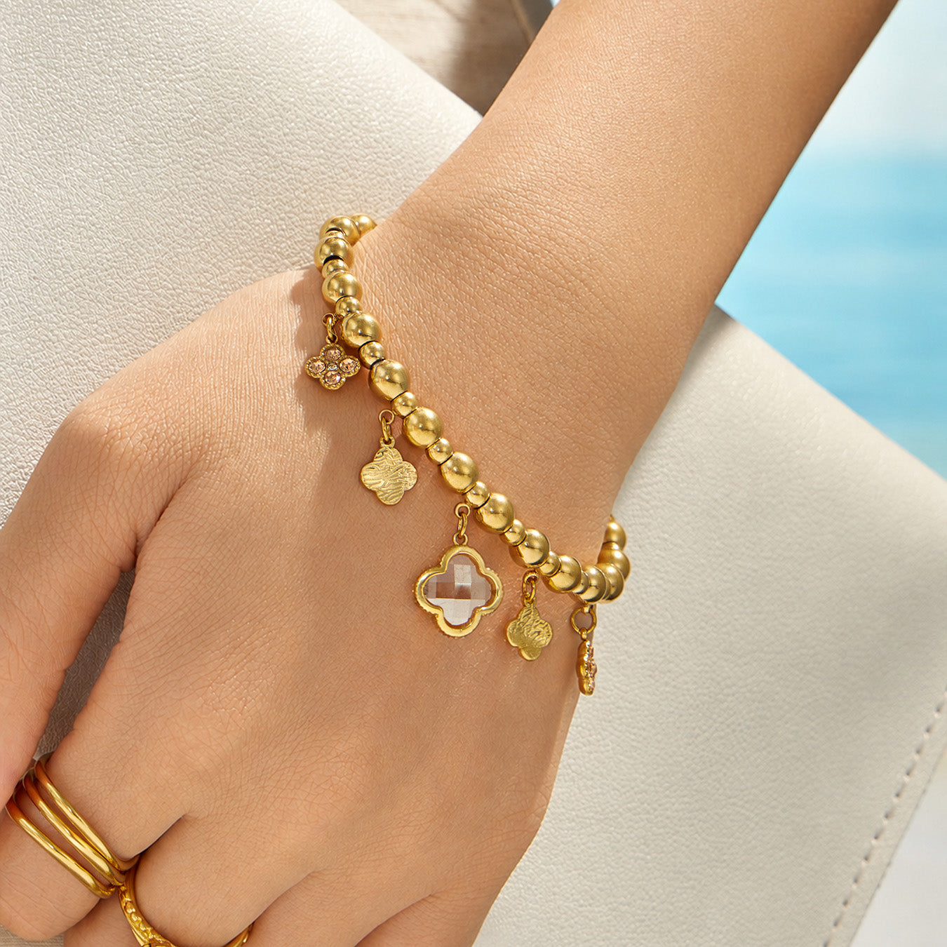 Champagne four-leaf clover charm bracelet worn on a model wrist with a neutral outfit