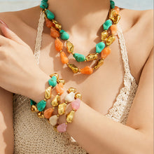 Model wearing a chunky green and orange resin necklace with matching stacked bracelets